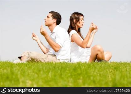 young couple sitting on grass and doing meditating
