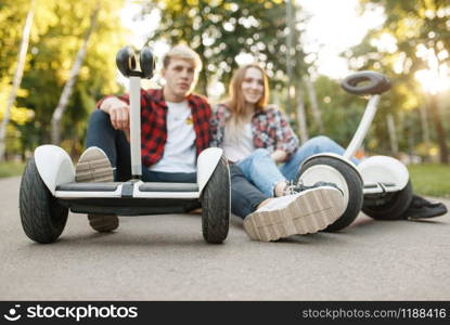 Young couple sitting on road with gyro board in summer park. Outdoor recreation with electric gyroboard. Eco transport with balance technology, electrical gyroscope vehicle