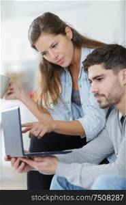young couple sitting on sofa at home looking in laptop