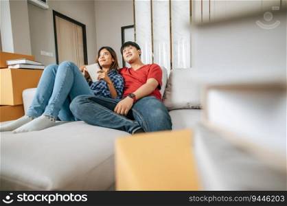 Young couple sitting on sofa checking on notebook while counting boxs after relocation in their new home, new house concept