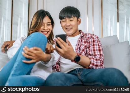 Young couple sitting on sofa in living room and use smartphone playing game together, they talk and laughing with happiness, happy family concept	