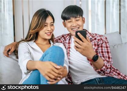 Young couple sitting on sofa in living room and use smartphone playing game together, they talk and laughing with happiness, happy family concept 