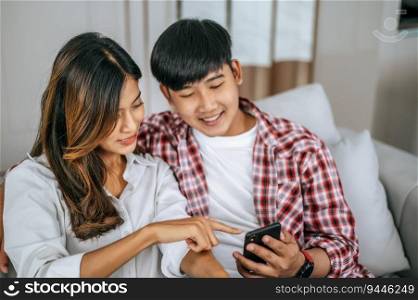 Young couple sitting on sofa in living room and use smartphone playing game together, they talk and laughing with happiness, happy family concept 