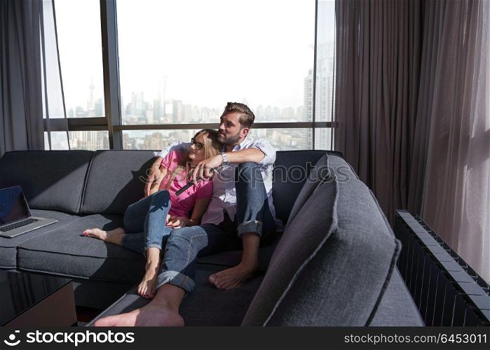Young couple sitting on sofa near the window watching television together at luxury home