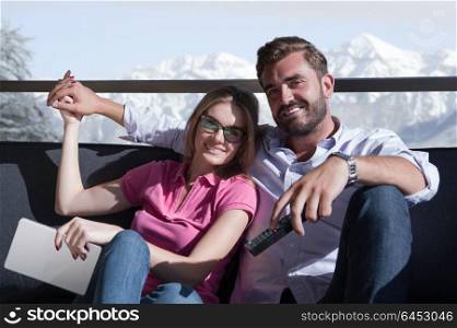 Young couple sitting on sofa near the window watching television together at luxury home