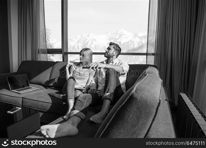 Young couple sitting on sofa near the window watching television together at luxury home. Young couple watching television