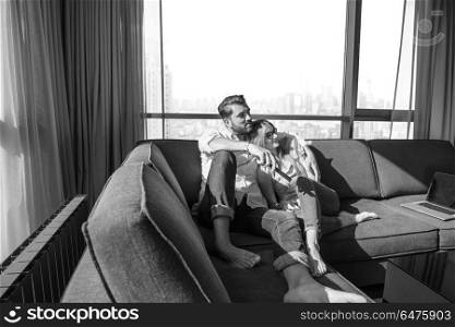 Young couple sitting on sofa near the window watching television together at luxury home. Young couple watching television