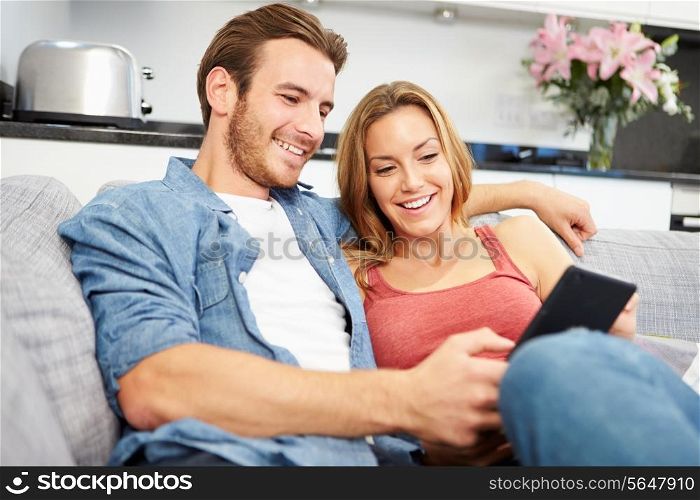 Young Couple Sitting On Sofa Using Digital Tablet