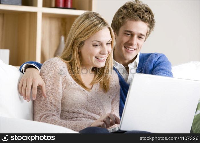 Young Couple Sitting On Sofa Using Laptop