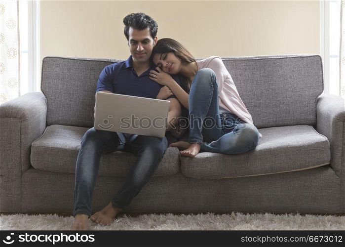 Young couple sitting on sofa using laptop at home