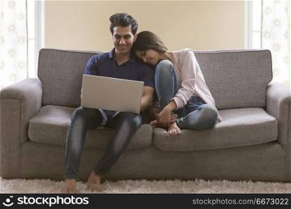Young couple sitting on sofa using laptop at home