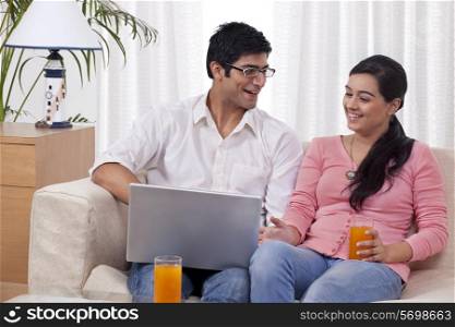 Young couple sitting on sofa using laptop with juice