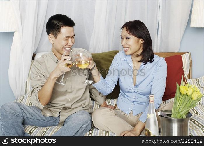 Young couple sitting on the bed toasting with wineglasses