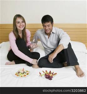 Young couple sitting on the bed with plates of salad in front of them