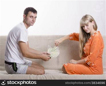 Young couple sitting on the couch, facing each other. The husband thinks the salary received, wife pulling one banknote