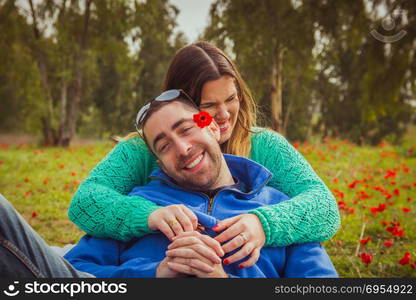 Young couple sitting on the grass in a field of red poppies and smiling and laughing at each other