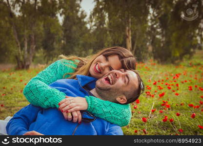 Young couple sitting on the grass in a field of red poppies and smiling and laughing at each other