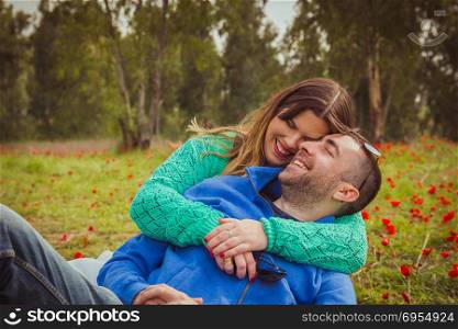 Young couple sitting on the grass in a field of red poppies and smiling and laughing at each other