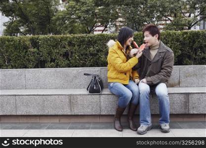 Young couple sitting on the ledge eating watermelon