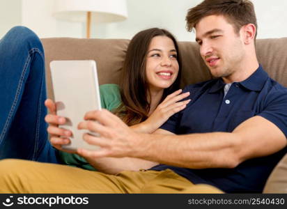 Young couple sitting on the sofa and watching something on a tablet