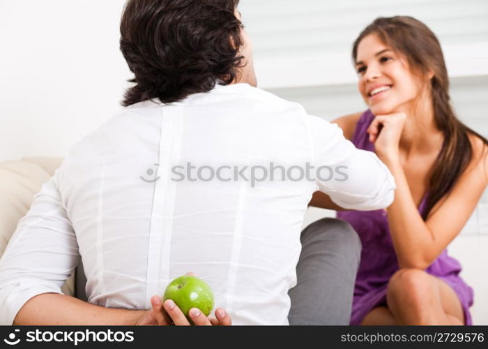 young couple sitting on the sofa,man hiding fruit from his girlfriend