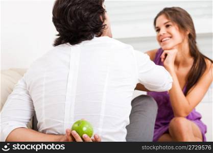 young couple sitting on the sofa,man hiding fruit from his girlfriend