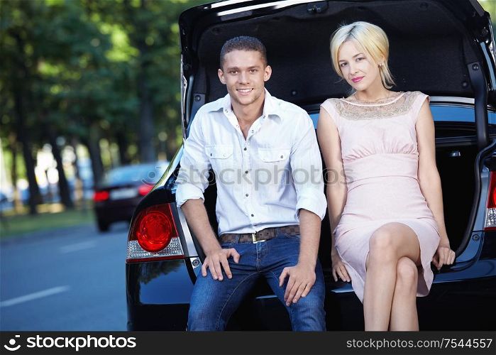 Young couple sitting on the trunk of a car
