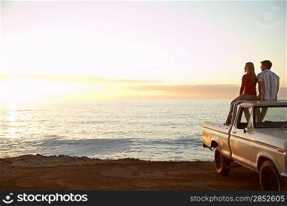 Young couple sitting on van parked in front of ocean