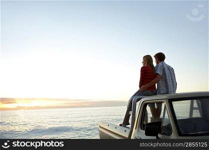 Young couple sitting on van parked in front of ocean