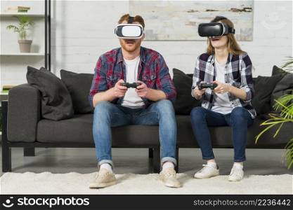 young couple sitting sofa using virtual reality glasses playing video game with joystick