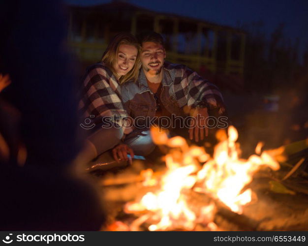 Young Couple Sitting with friends Around Campfire on The Beach At Night drinking beer. Couple enjoying with friends at night on the beach