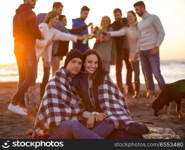 Young Couple Sitting with friends Around Campfire on The Beach At sunset drinking beer. Couple enjoying with friends at sunset on the beach