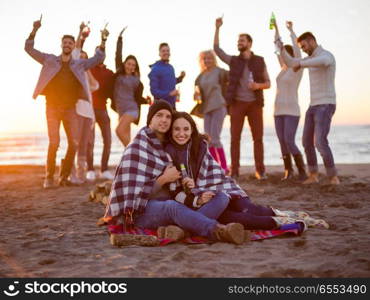 Young Couple Sitting with friends Around Campfire on The Beach At sunset drinking beer. Couple enjoying with friends at sunset on the beach