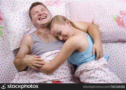 Young couple sleeping in bed under the belt blanket. The girl lay down on the guy&#39;s shoulder. About happily laugh. Photo made at the top