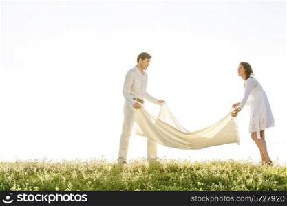 Young couple spreading picnic blanket on grass during sunny day