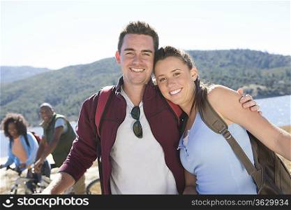 Young couple stand at lakeside man with his arm around the woman