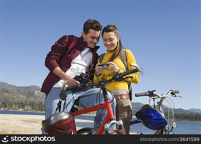 Young couple stand with mountain bike looking at screen of camera