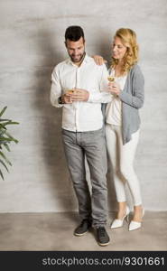 Young couple standing by wall and holding glasses of white wine in hands