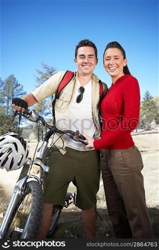 Young couple standing in field with mountain bike.