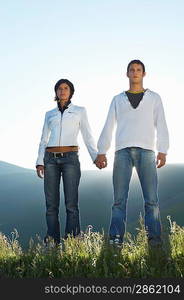 Young couple standing in mountain field looking at view front view low angle view