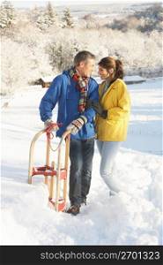 Young Couple Standing In Snowy Landscape Holding Sledge