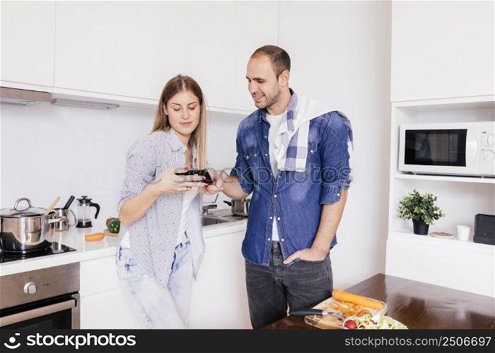 young couple standing kitchen using mobile phone while cooking food