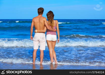 Young couple standing looking at the beach rear back view