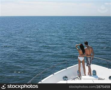 Young couple standing on bow of yacht looking at seascape back view