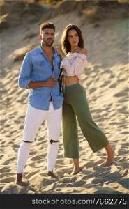 Young couple standing on the sand of the beach wearing casual clothes.. Young couple standing on the sand of the beach