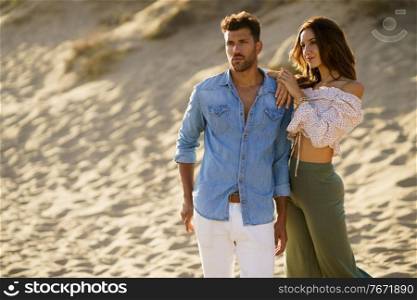 Young couple standing on the sand of the beach wearing casual clothes.. Young couple standing on the sand of the beach