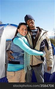 Young couple standing outdoors with tents in background.