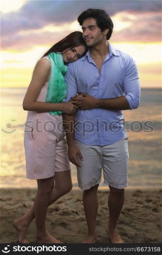 Young couple standing together on beach at sunset