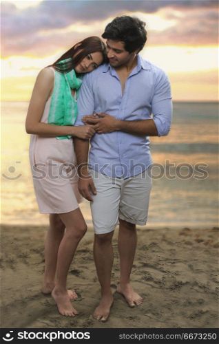 Young couple standing together on beach at sunset