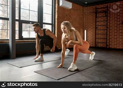 Young couple stretching legs at gym. Fit man and woman doing lunge exercises at pilates training workout class indoor. Young couple stretching legs at training gym class
